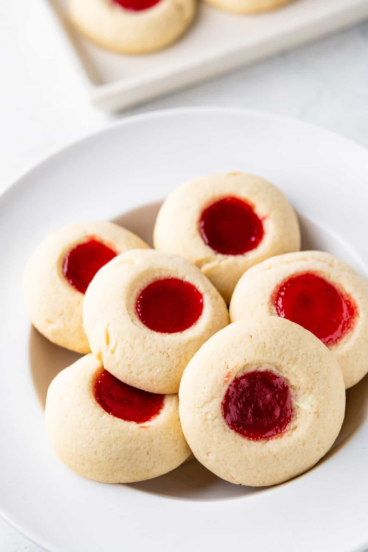 A white plate is stacked with strawberry thumbprint cookies.