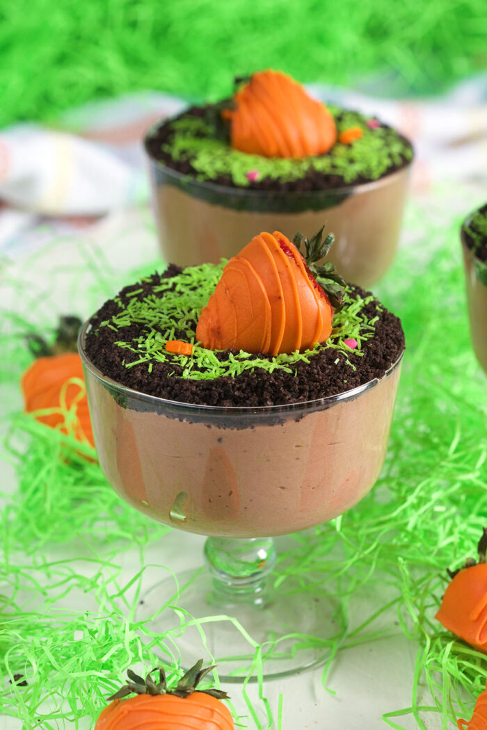 Two Easter dirt cups are garnished with orange coated chocolate strawberries.