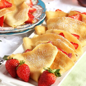 French Crepes stuffed with strawberries on a white platter with fresh berries