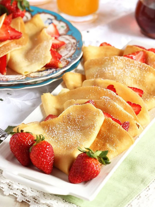 French Crepes stuffed with strawberries on a white platter with fresh berries