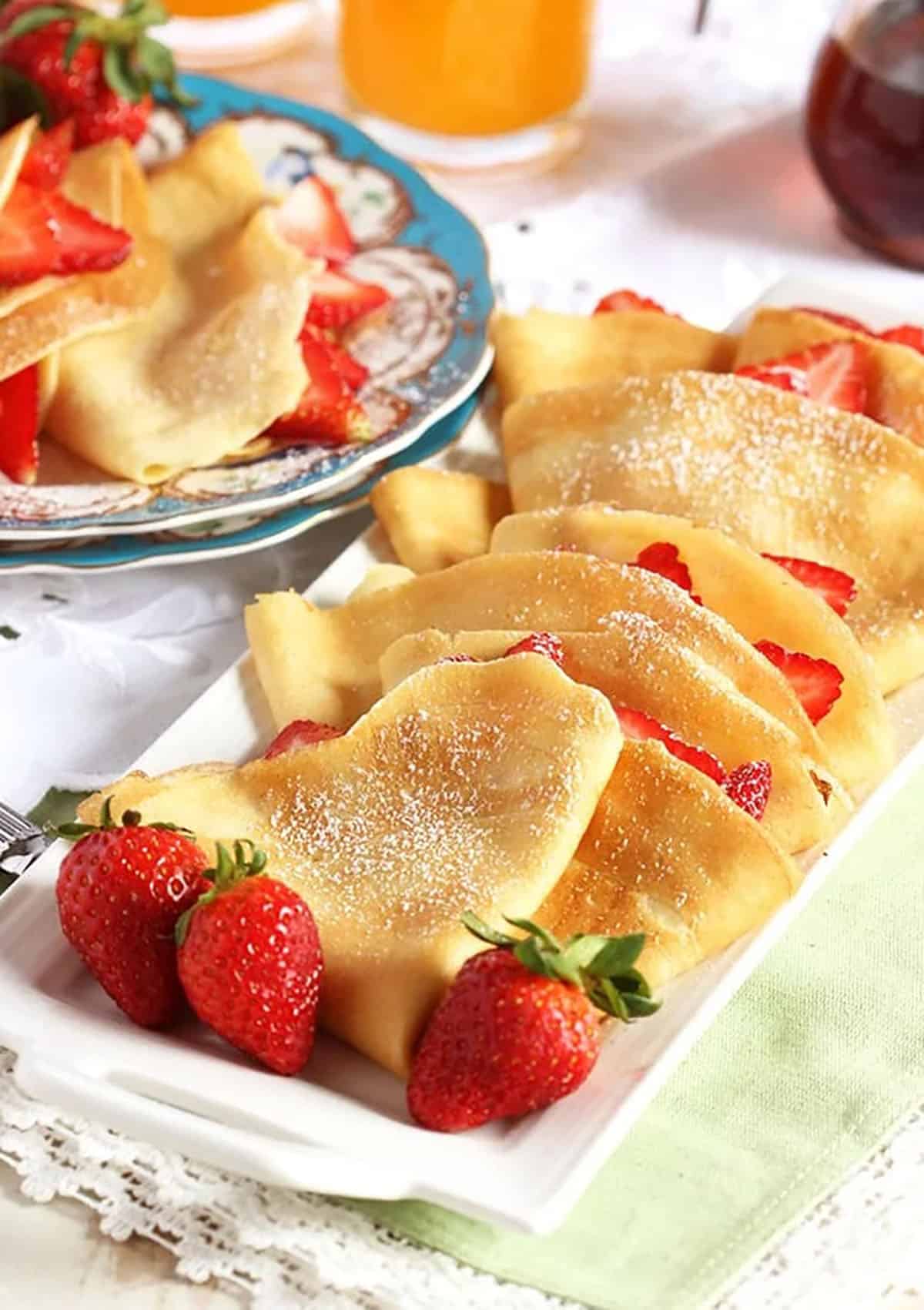 French Crepes stuffed with strawberries on a white platter with fresh berries 