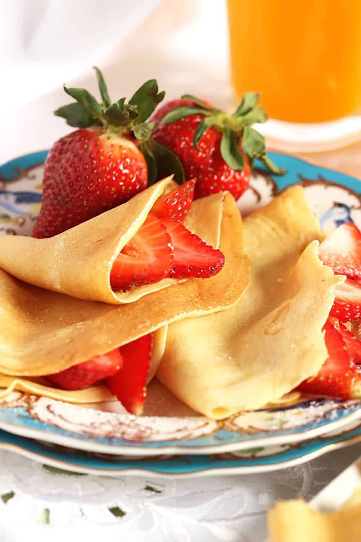 French Crepes stuffed with sliced strawberries on a blue and white plate.
