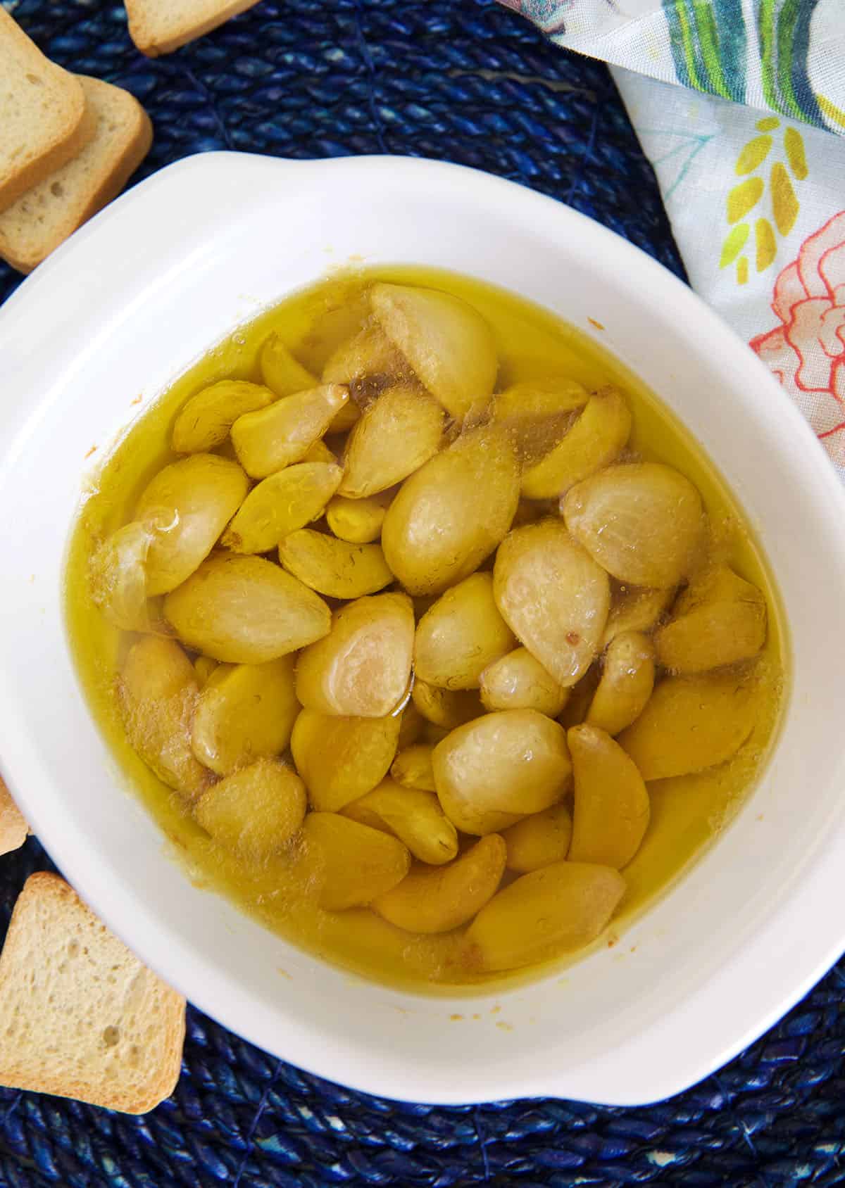 A white baking dish is filled with olive oil and garlic cloves.