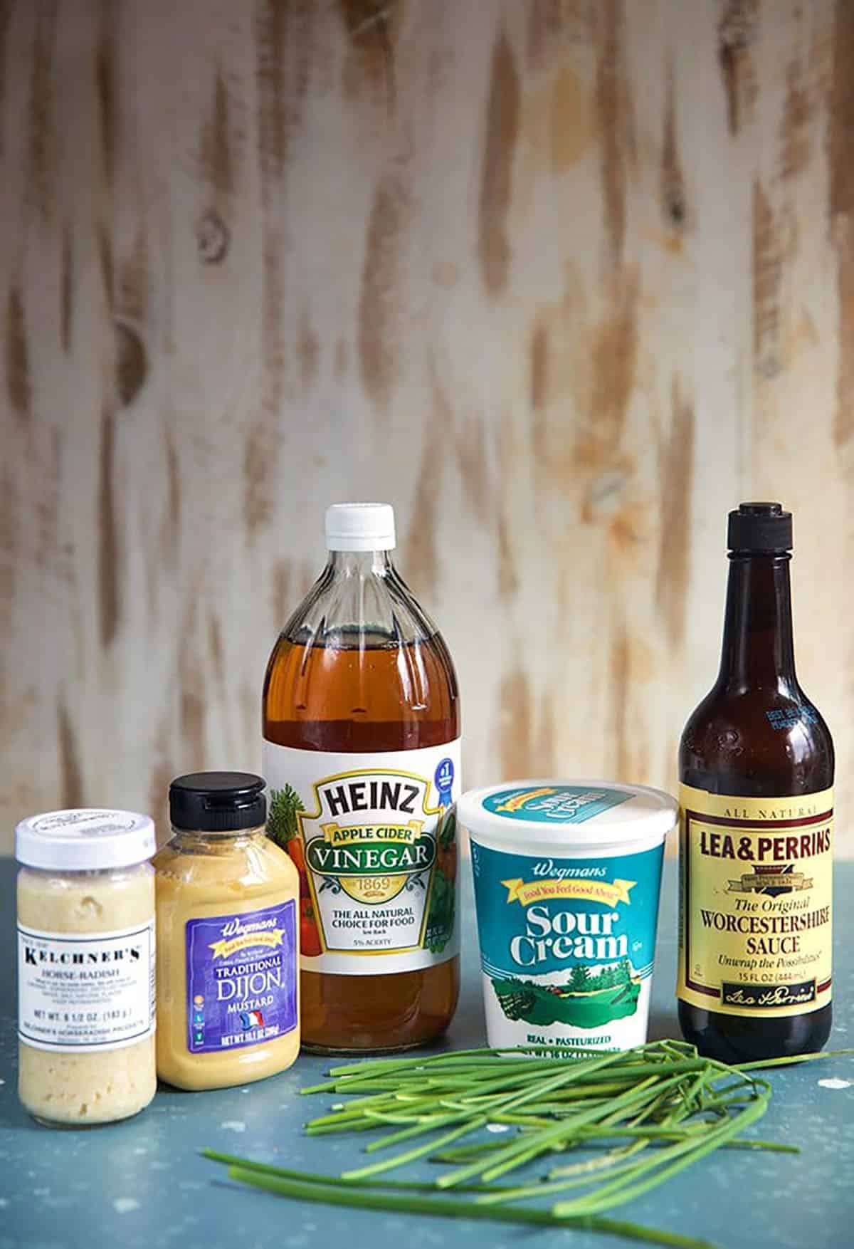 Ingredients for Creamy Horseradish Sauce, a bottle of horseradish, dijon mustard, apple cider vinegar, sour cream Worcestershire sauce and chives.