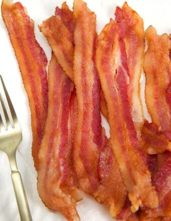 Several strips of cooked bacon are presented by a fork.