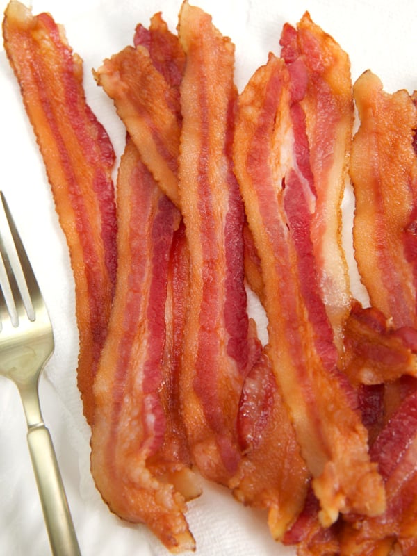 Several strips of cooked bacon are presented by a fork.