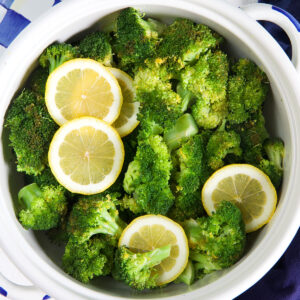 A white pot is filled with steamed broccoli and lemon slices.