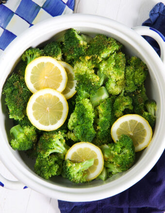 A white pot is filled with steamed broccoli and lemon slices.