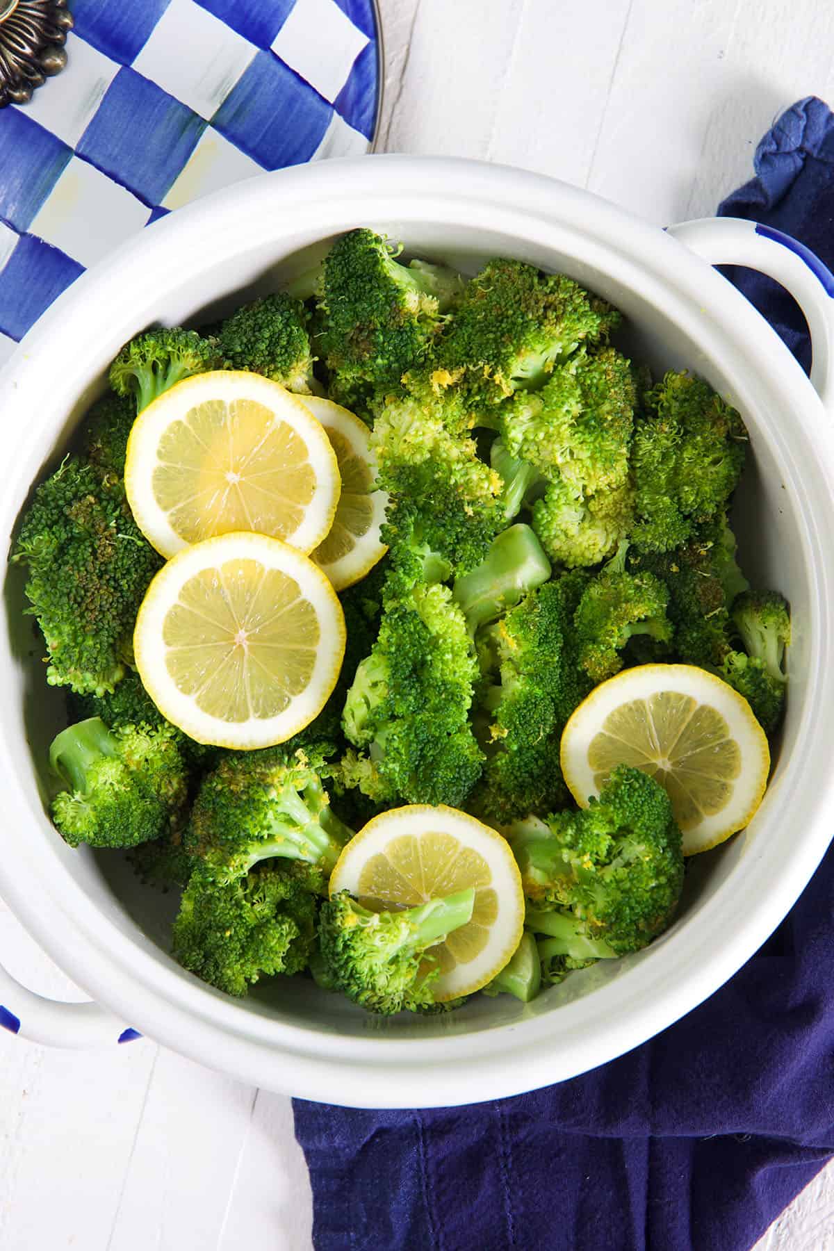 A white pot is filled with steamed broccoli and lemon slices.