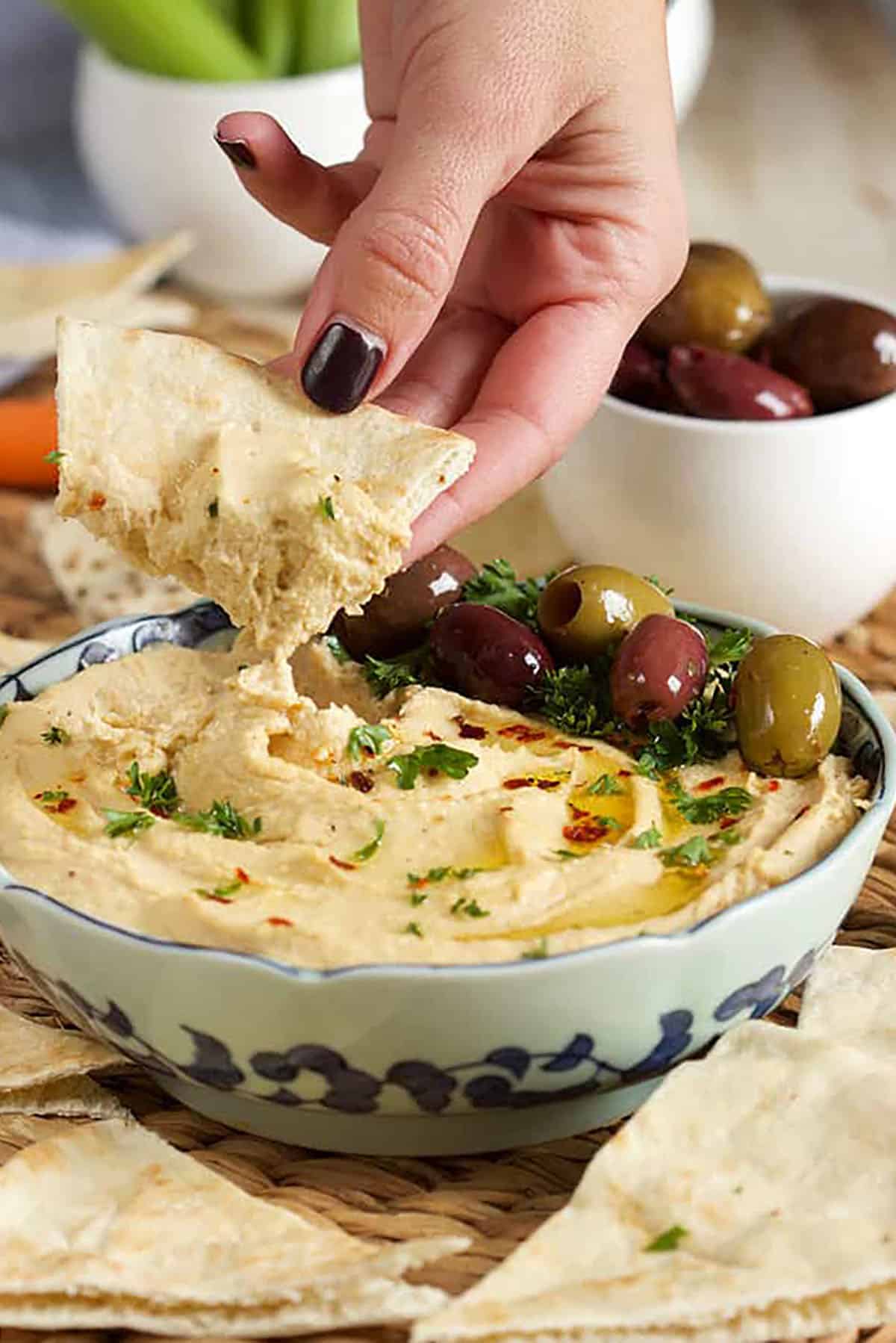 Hummus in a bowl with a hand dipping a pita wedge into it.