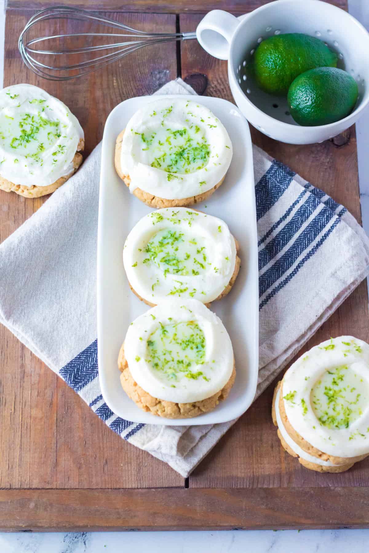 Several frosted key lime cookies are presented on and around a rectangular white plate.