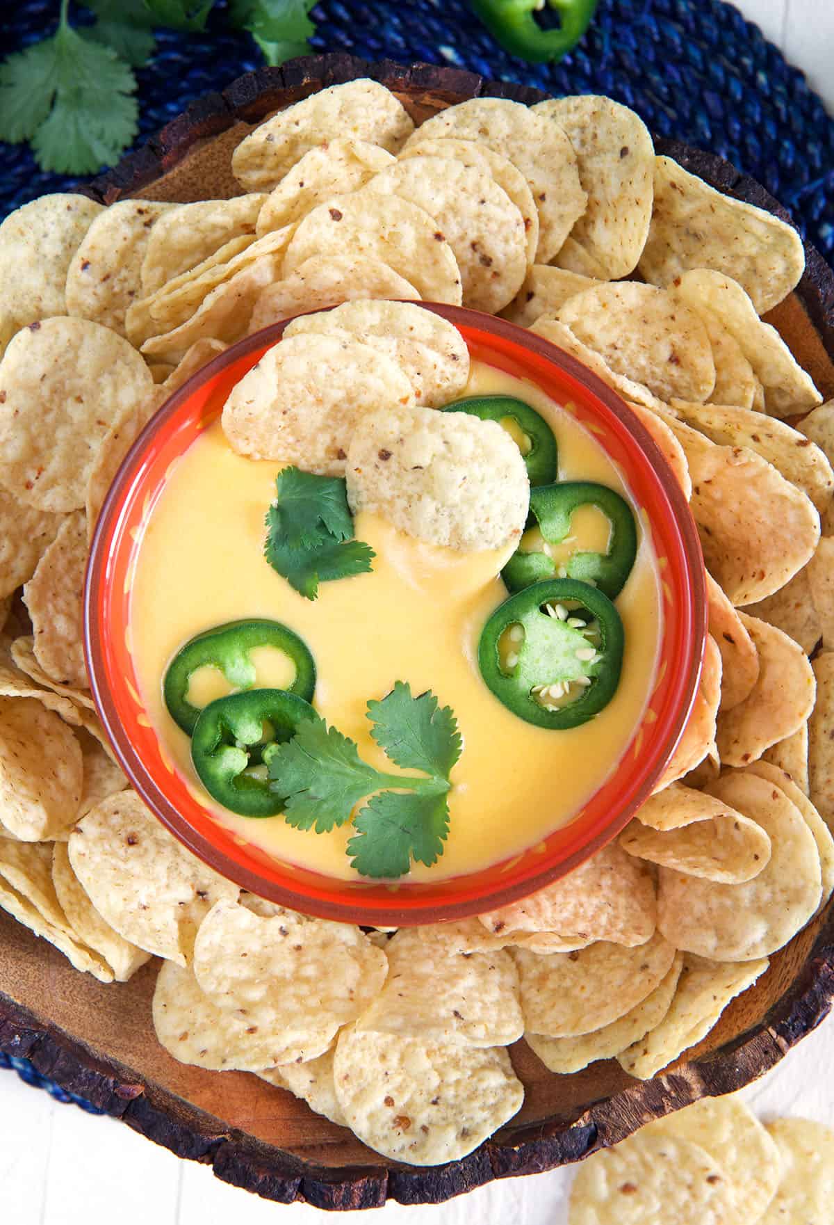 A small bowl is filled with nacho cheese and topped with jalapenos, and it's surrounded by round tortilla chips.