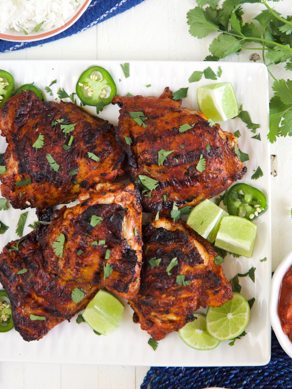 A square white platter is filled with cooked chicken thighs.