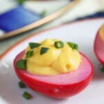 A red deviled egg is topped with chopped chives.
