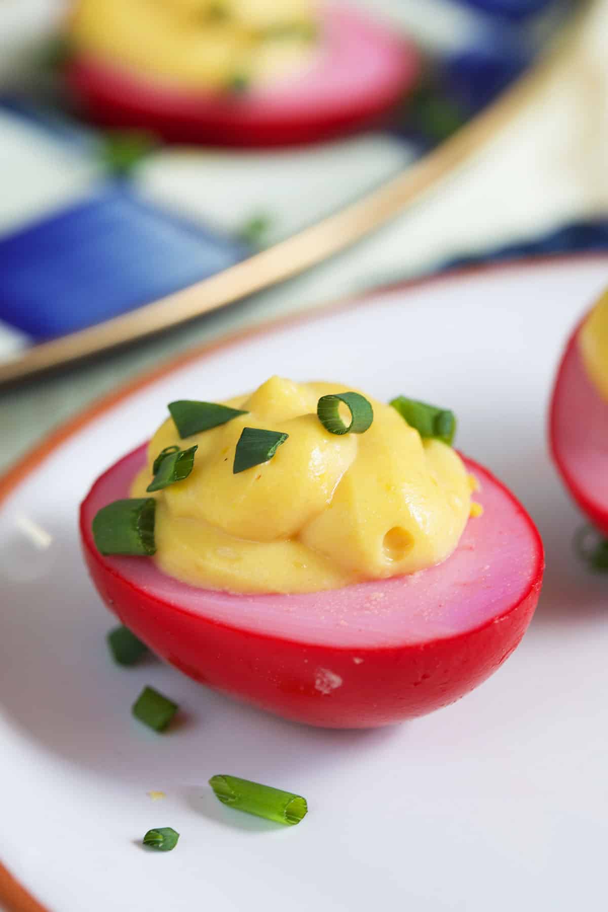 A red deviled egg is topped with chopped chives.