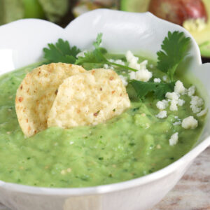 Chips, cheese, and cilantro are placed on top of a bowl of green salsa.