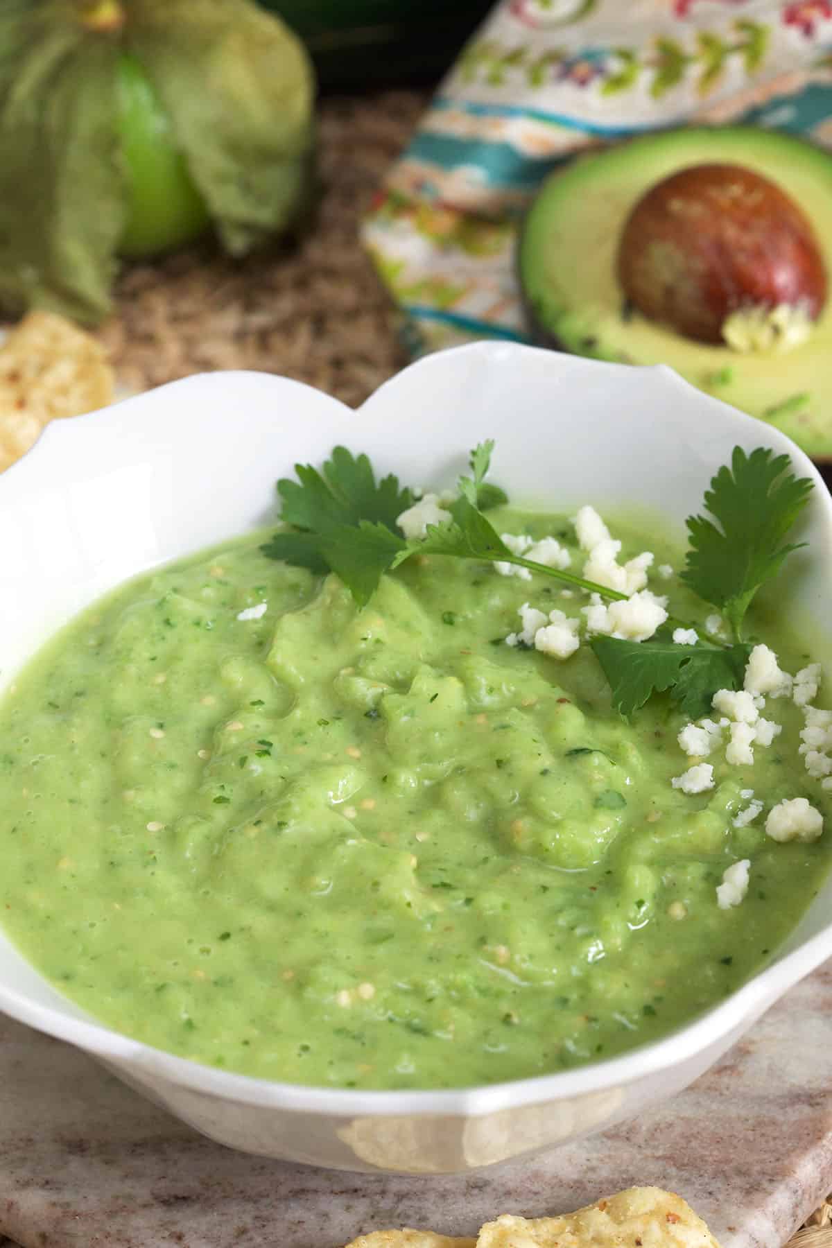 A white bowl is filled with fresh green avocado salsa, crumbled cojita cheese, and cilantro.