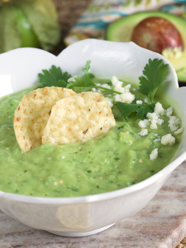 Chips, cheese, and cilantro are placed on top of a bowl of green salsa.