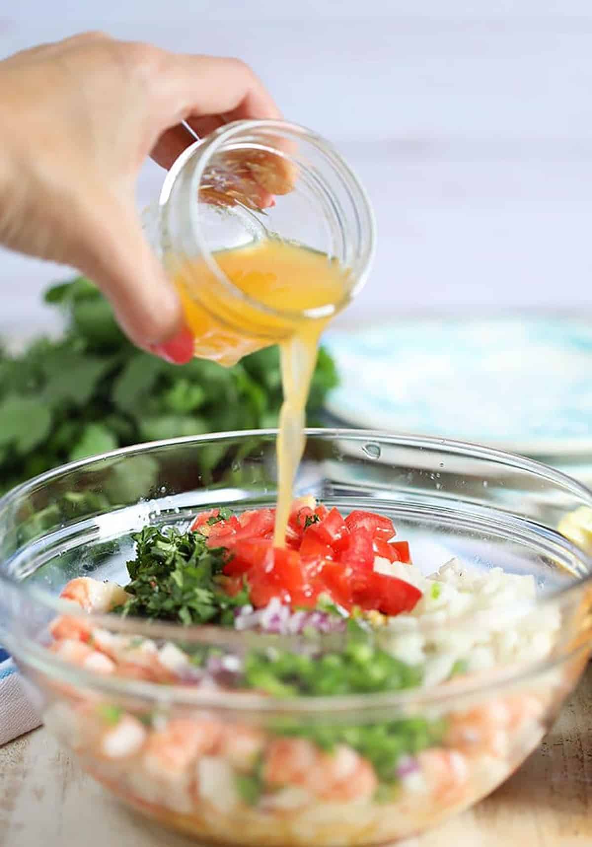 Ingredients for Shrimp Ceviche in a glass bowl with dressing being poured.