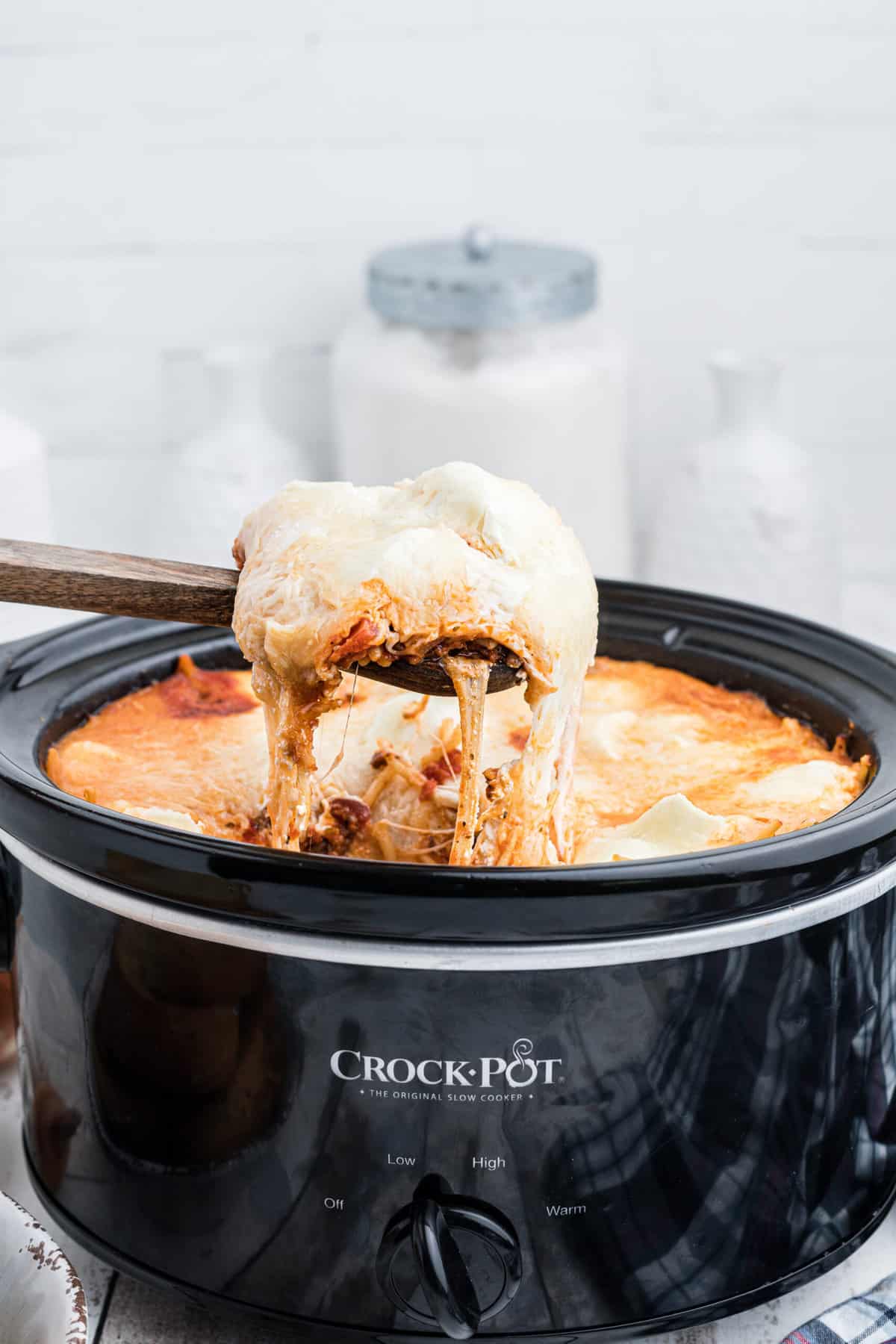 A cheesy serving of spaghetti is being lifted from the Crockpot.