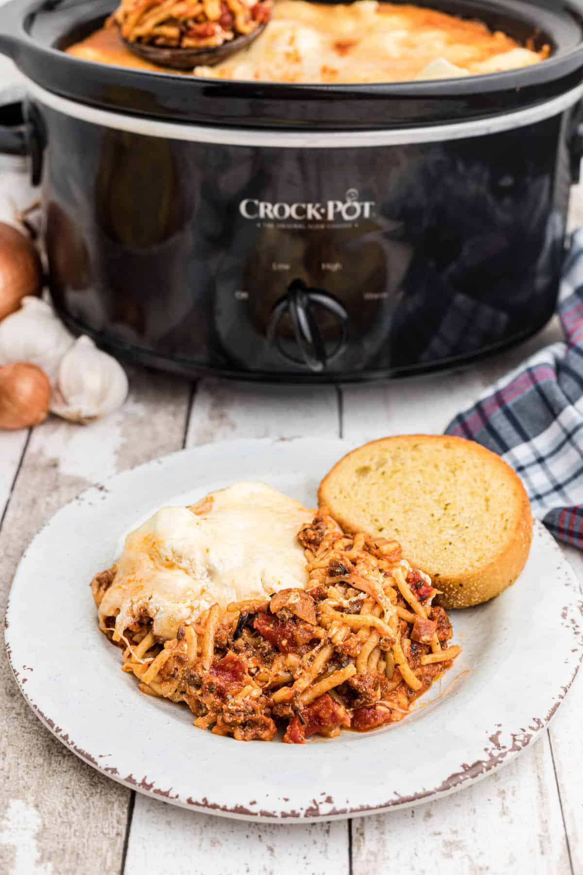 A plate topped with spaghetti and a slice of bread is placed next to a full Crockpot.