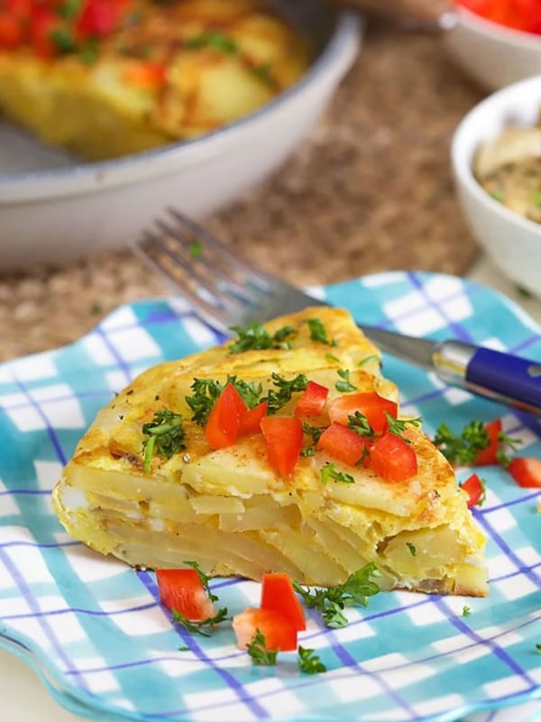 Spanish Tortilla slice on a plaid plate with bell pepper on top.