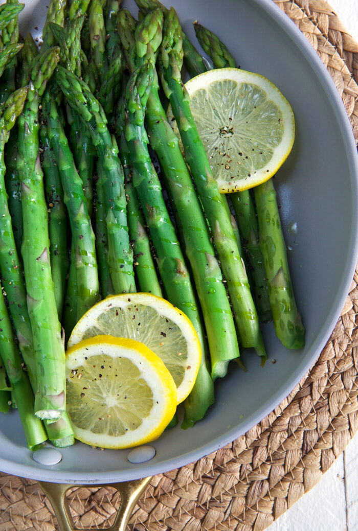 Several lemon slices are placed in a skillet with cooked asparagus. 