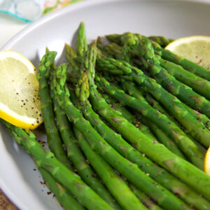 A plate contains a serving of steamed asparagus with lemon slices.