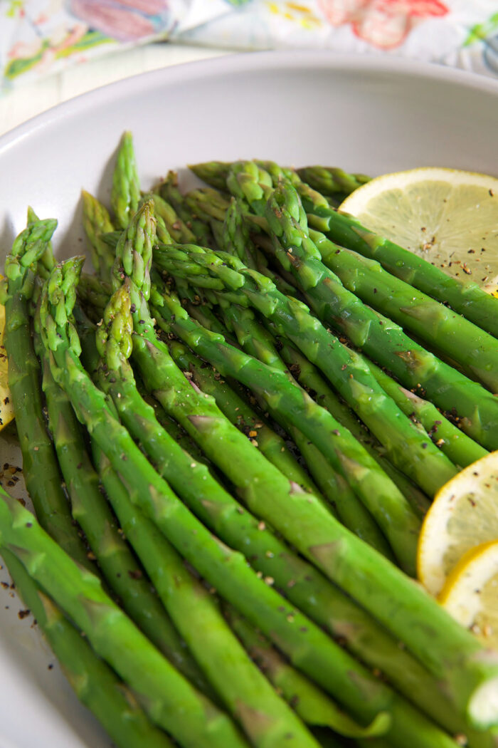 Steamed asparagus and lemon slices are fully cooked in a skillet.