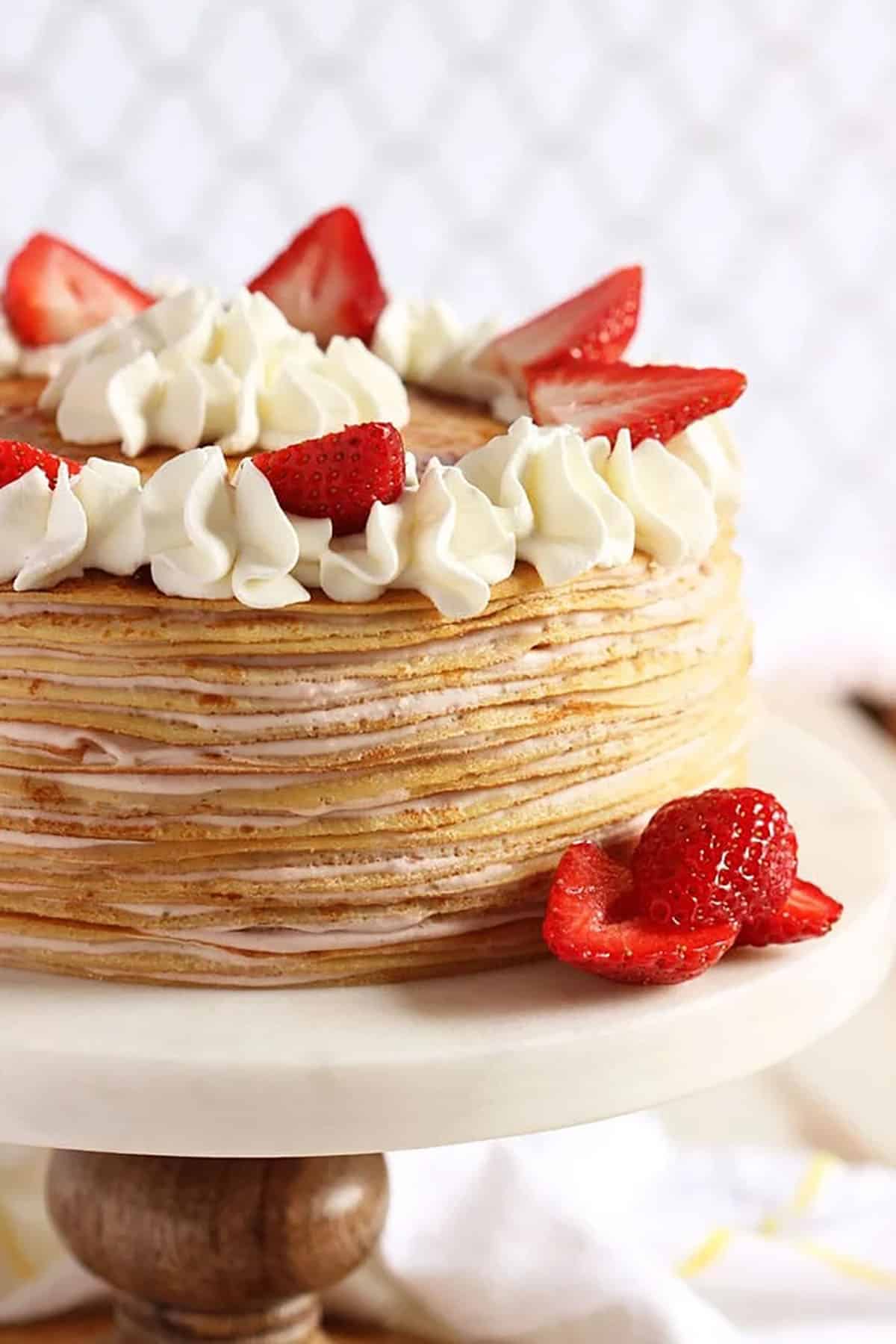 strawberry crepe cake on a pedestal with berries and cream
