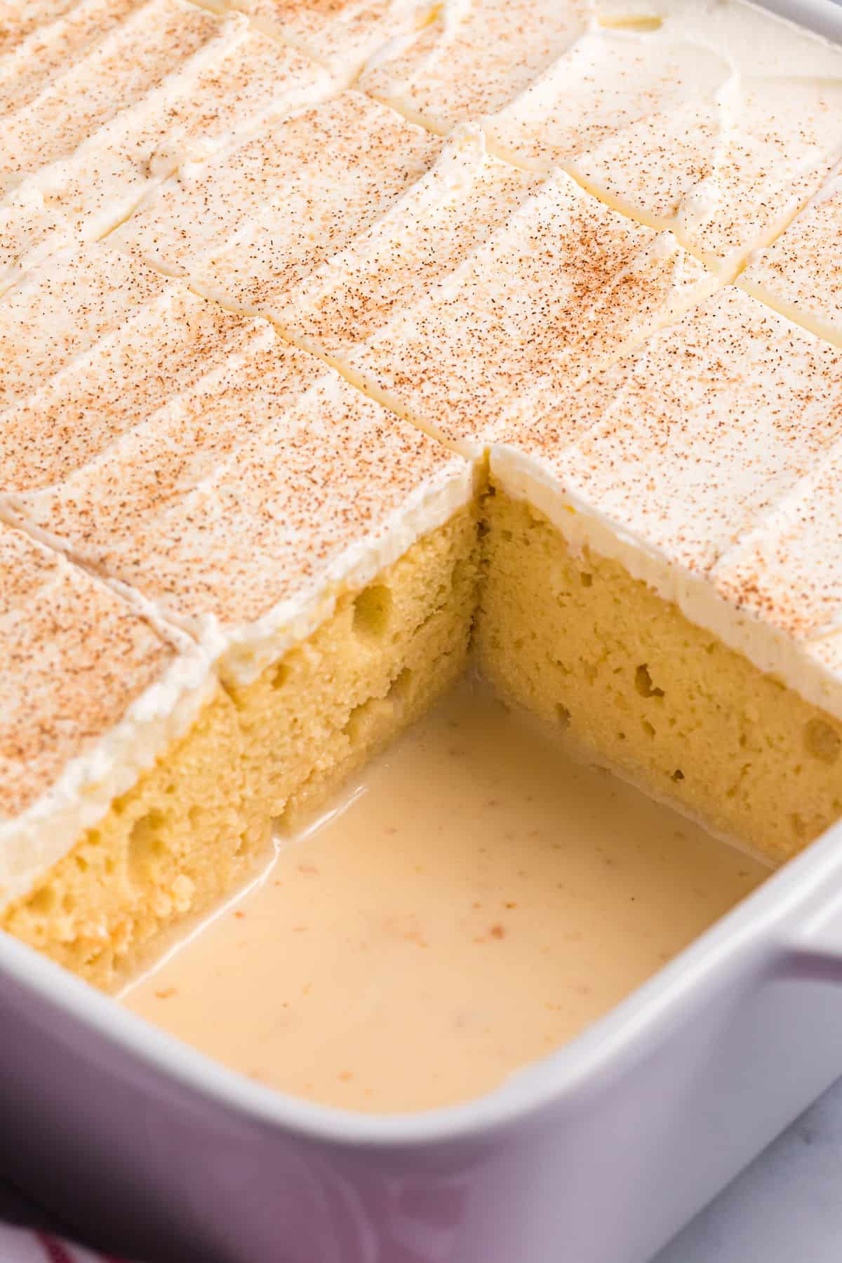 A slice of tres leches cake is missing from the baking dish.