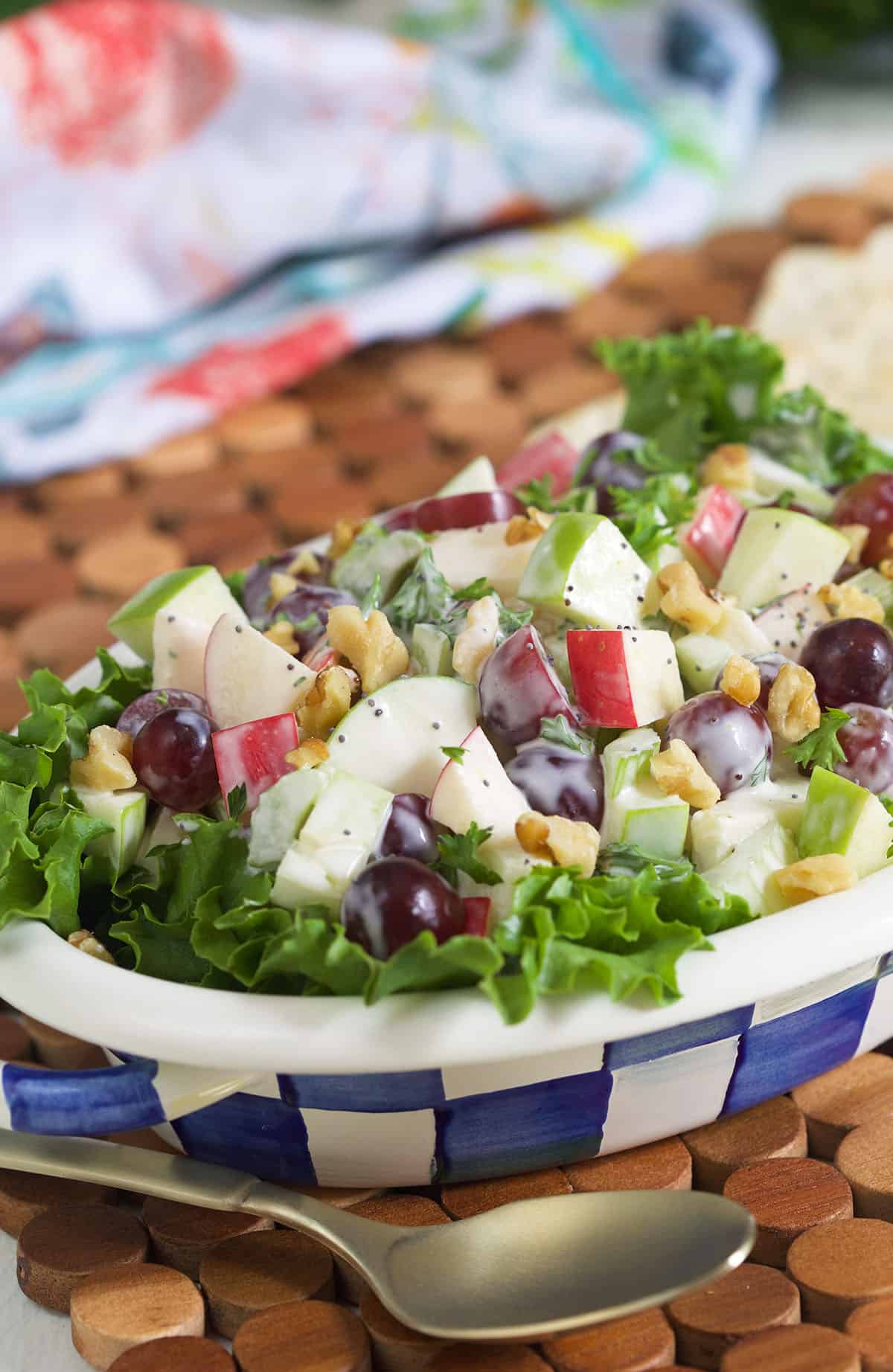 A blue and white checkered bowl is filled with freshly tossed Waldorf salad.