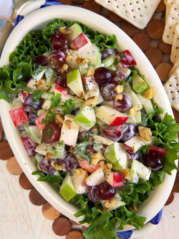 An ovular white bowl is filled with waldorf salad.
