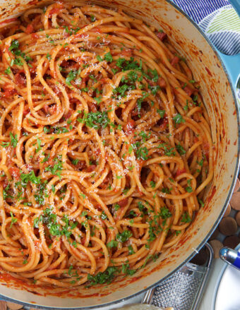 A white pot is filled with sauce coated pasta and fresh parsley.