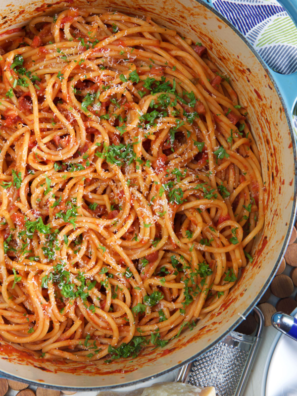 A white pot is filled with sauce coated pasta and fresh parsley.