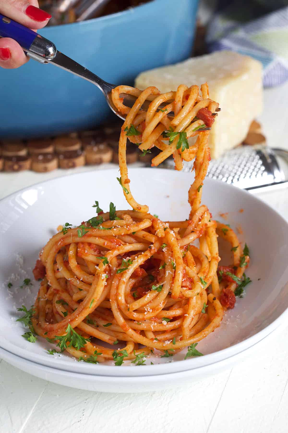 A fork has twirled pasta and is held above a white bowl.