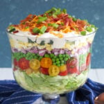 A seven layer salad is prepared in a trifle dish on a white countertop.