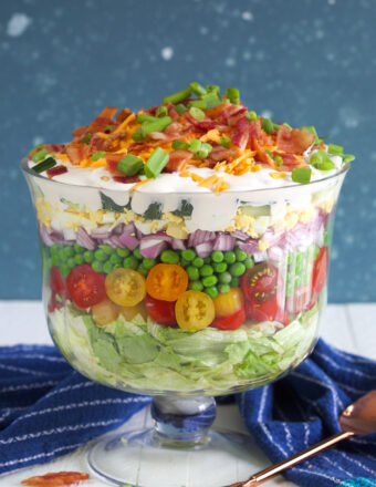 A seven layer salad is prepared in a trifle dish on a white countertop.