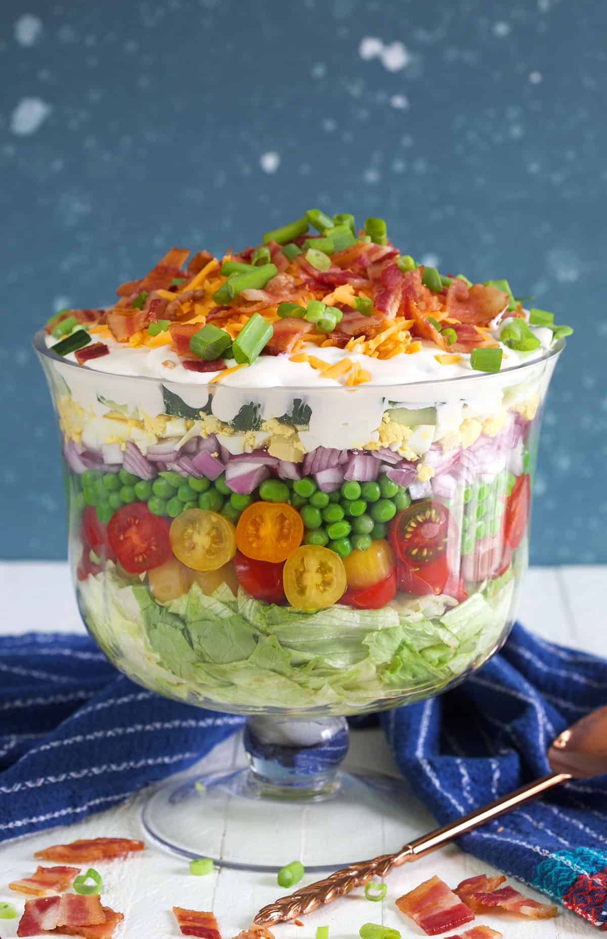 A seven layer salad is prepared in a trifle dish on a white countertop. 