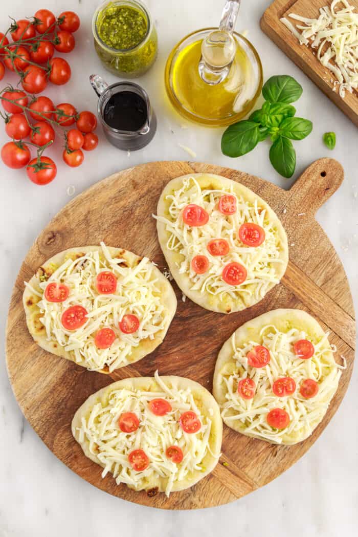 Four small uncooked pizzas are placed on a round wooden cutting board.