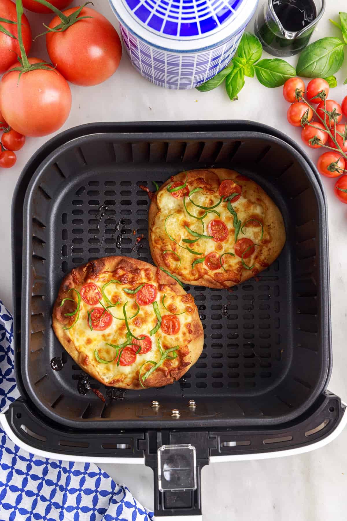 Two cooked pizzas are in the basket of an air fryer.
