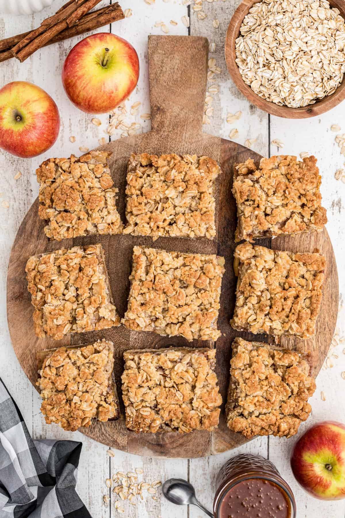Nine apple pie bars are placed on a wooden cutting board.