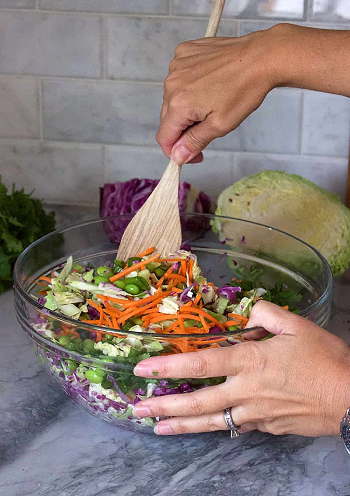 Asian coleslaw being mixed with a spoon in a glass mixing bowl.