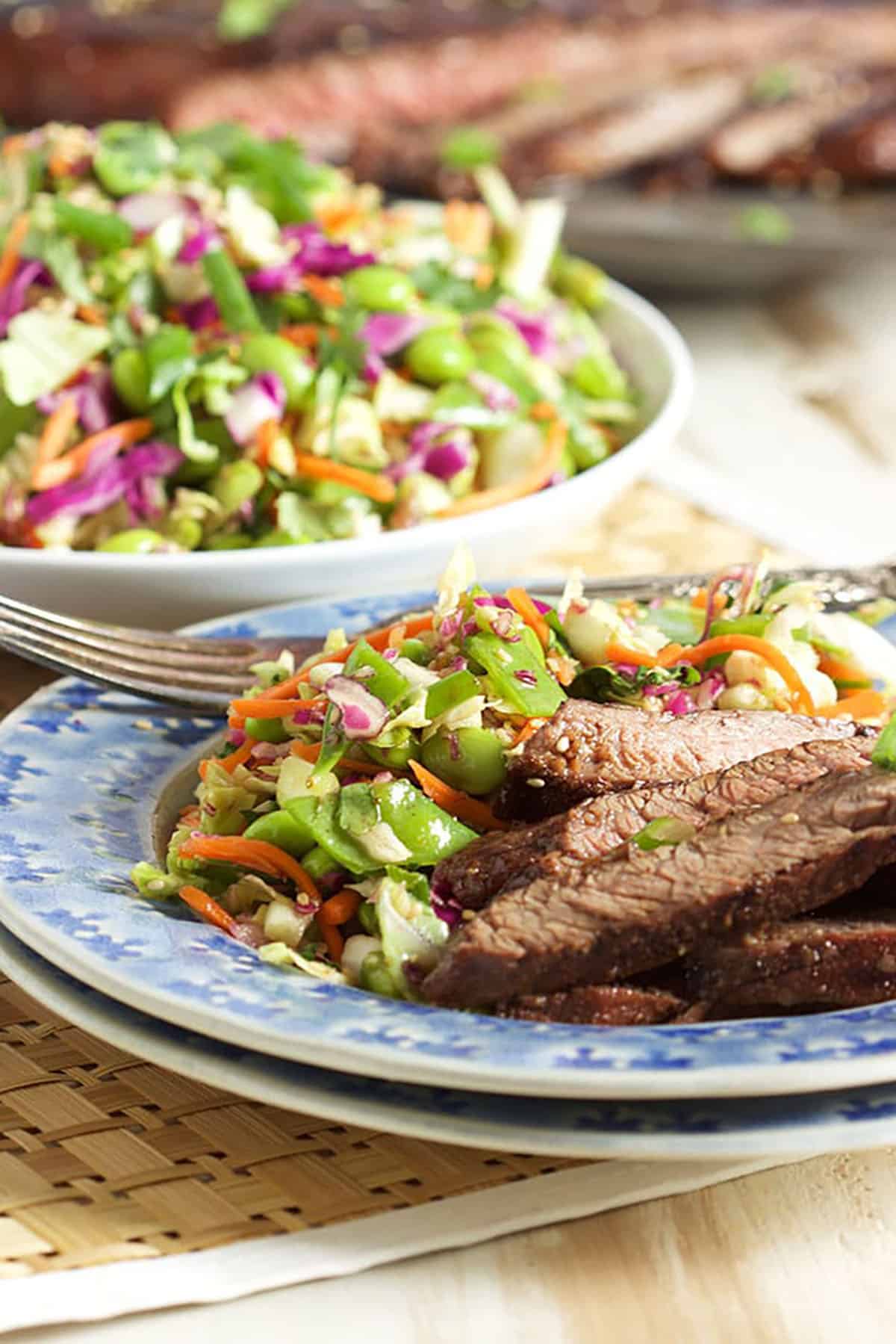 Asian coleslaw plated with sliced steak on a blue plate.