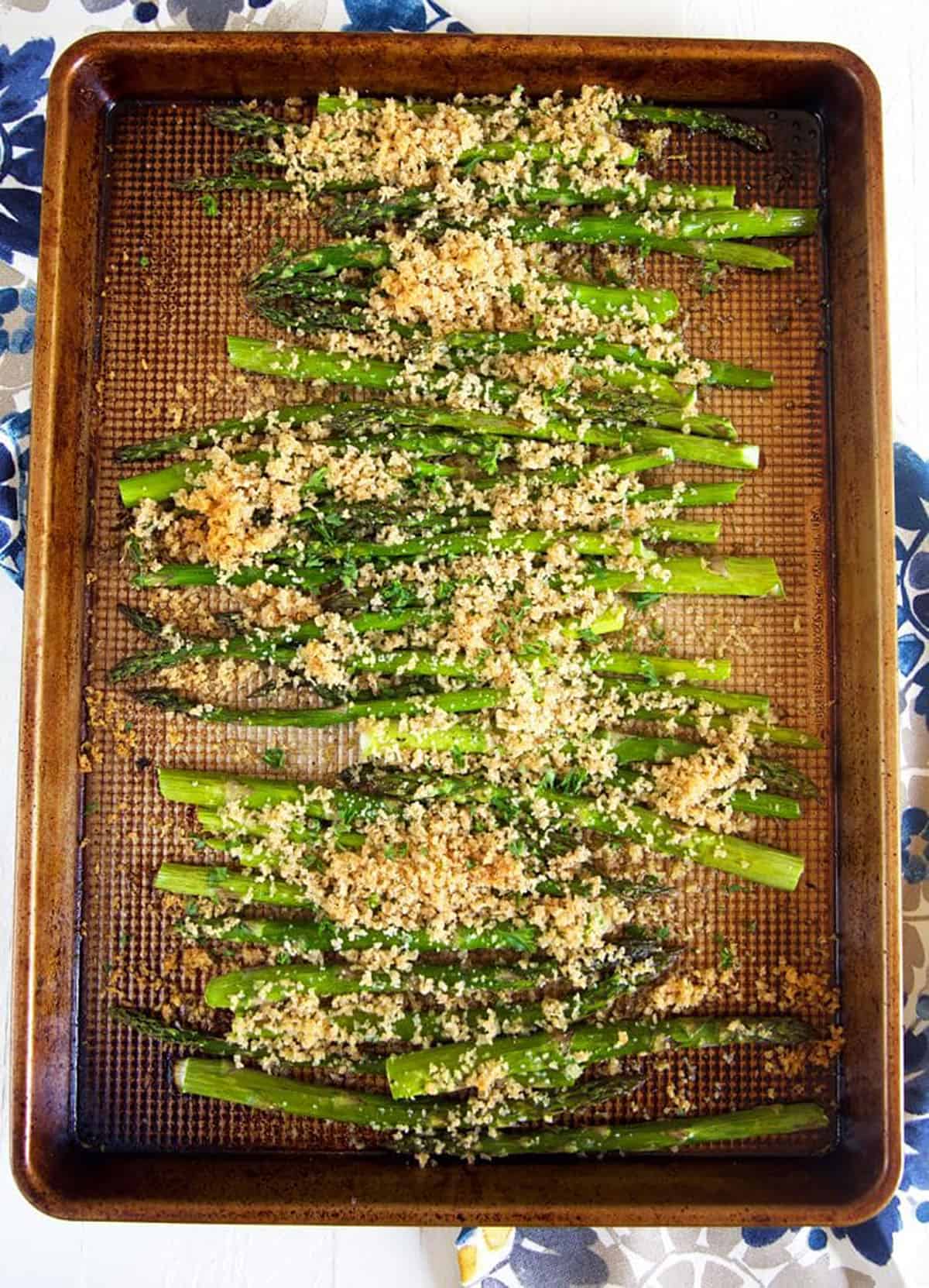Overhead shot of baked asparagus on a baking sheet with panko crumbs.