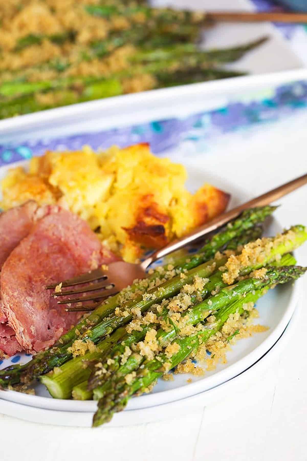 Baked asparagus on a plate with ham and pineapple casserole.