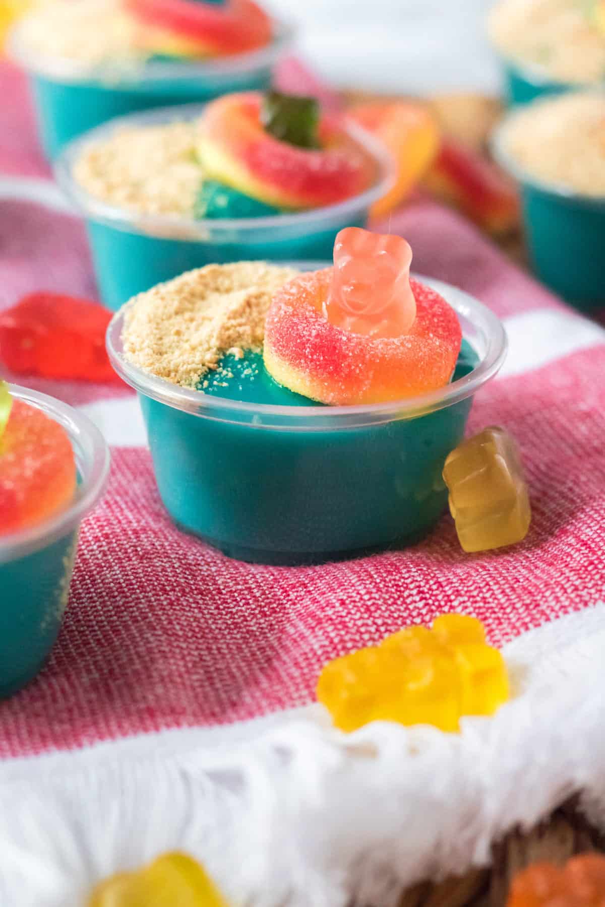 Extra gummy bears are scattered around a pudding shot on a tea towel.