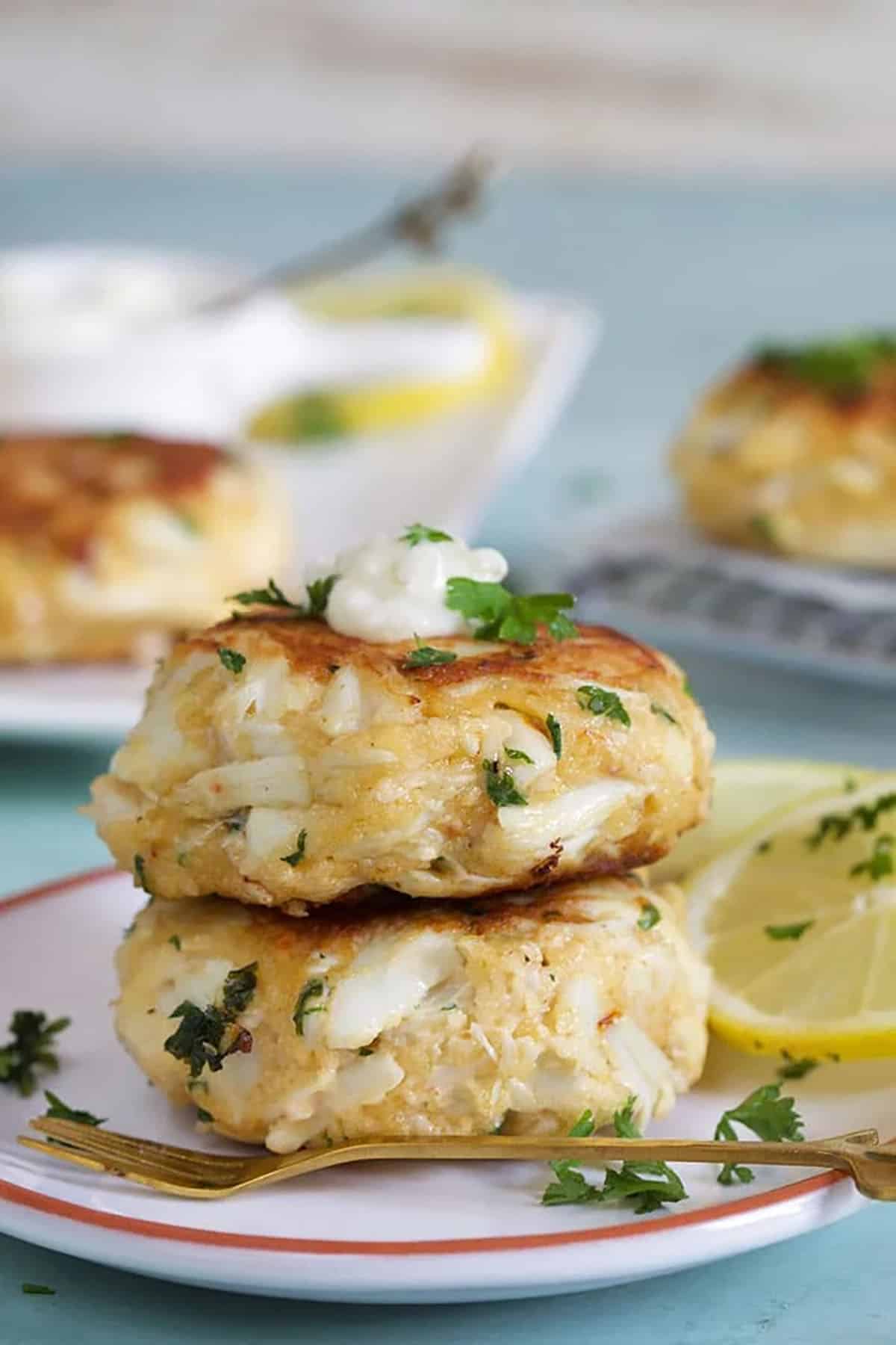 Two crab cakes stacked on a white plate with a dollop of tartar sauce on the top and a lemon slice.