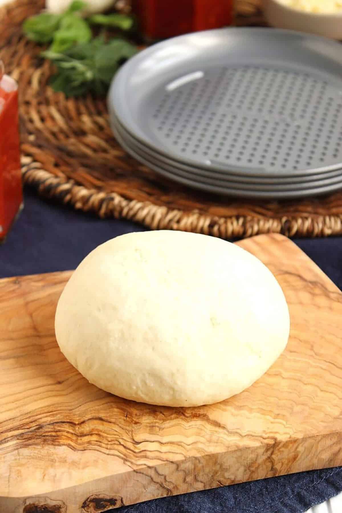 homemade pizza dough on an olive wood board with small pizza pans in the background.