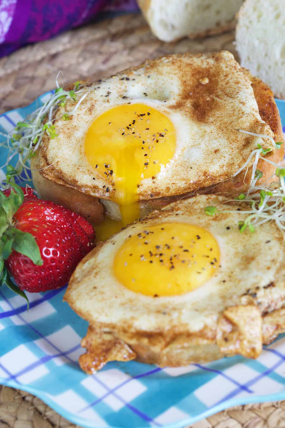 Two basted eggs on toast are presented on a white and blue plate.
